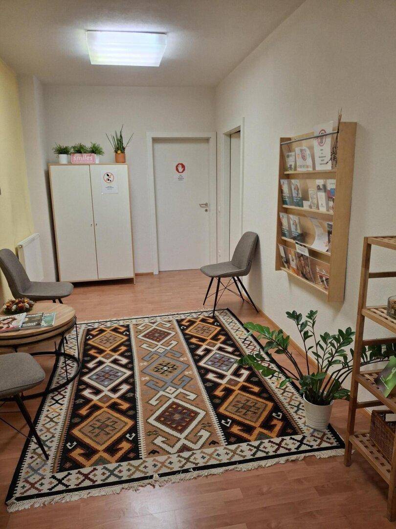 Gemütlicher Wartebereich mit Teppich, Pflanzen und Informationsmaterial für Besucher in angenehmer Umgebung.