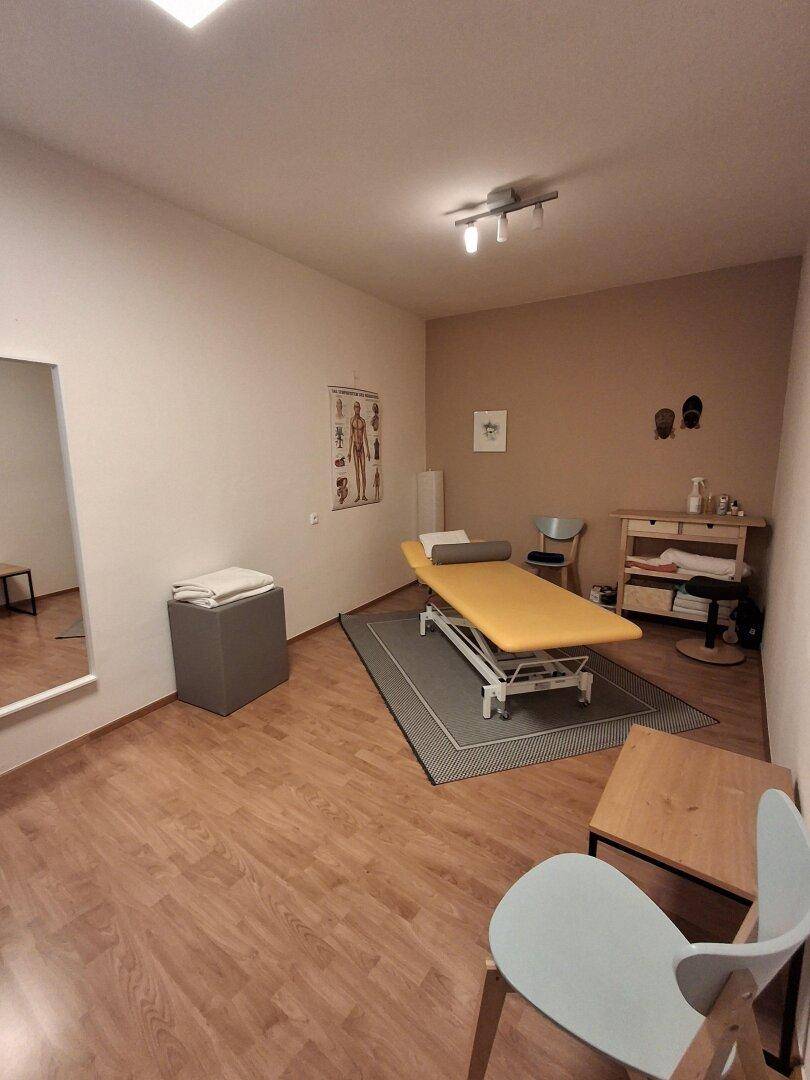 Therapieraum mit Liege, Spiegel und Stühlen, ideal für Behandlungen und Beratungen in ruhiger Atmosphäre.