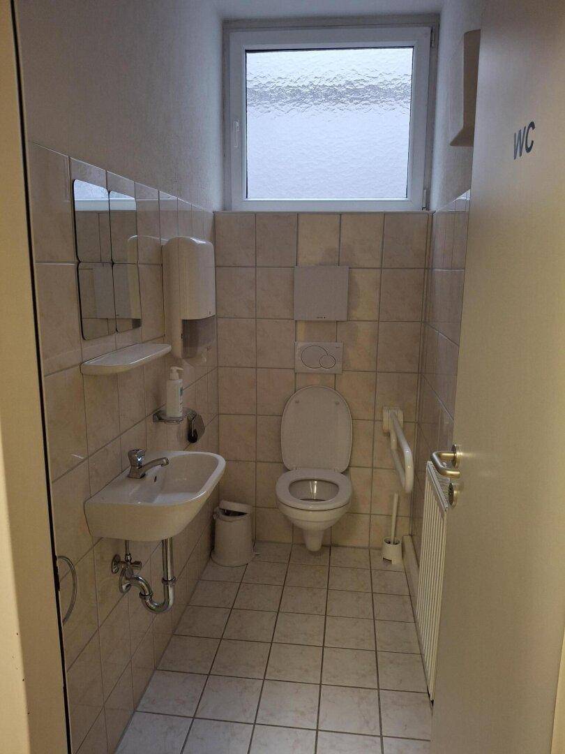 Saubere Gästetoilette mit Fenster, Waschbecken und Wand-WC, gut beleuchtet und funktional.