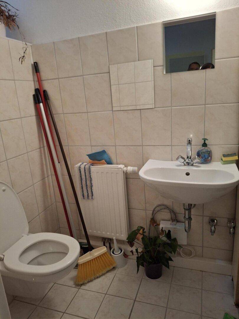 Kleine Toilette mit Fliesenboden, Waschbecken und Heizkörper, funktional eingerichtet und sauber gehalten.