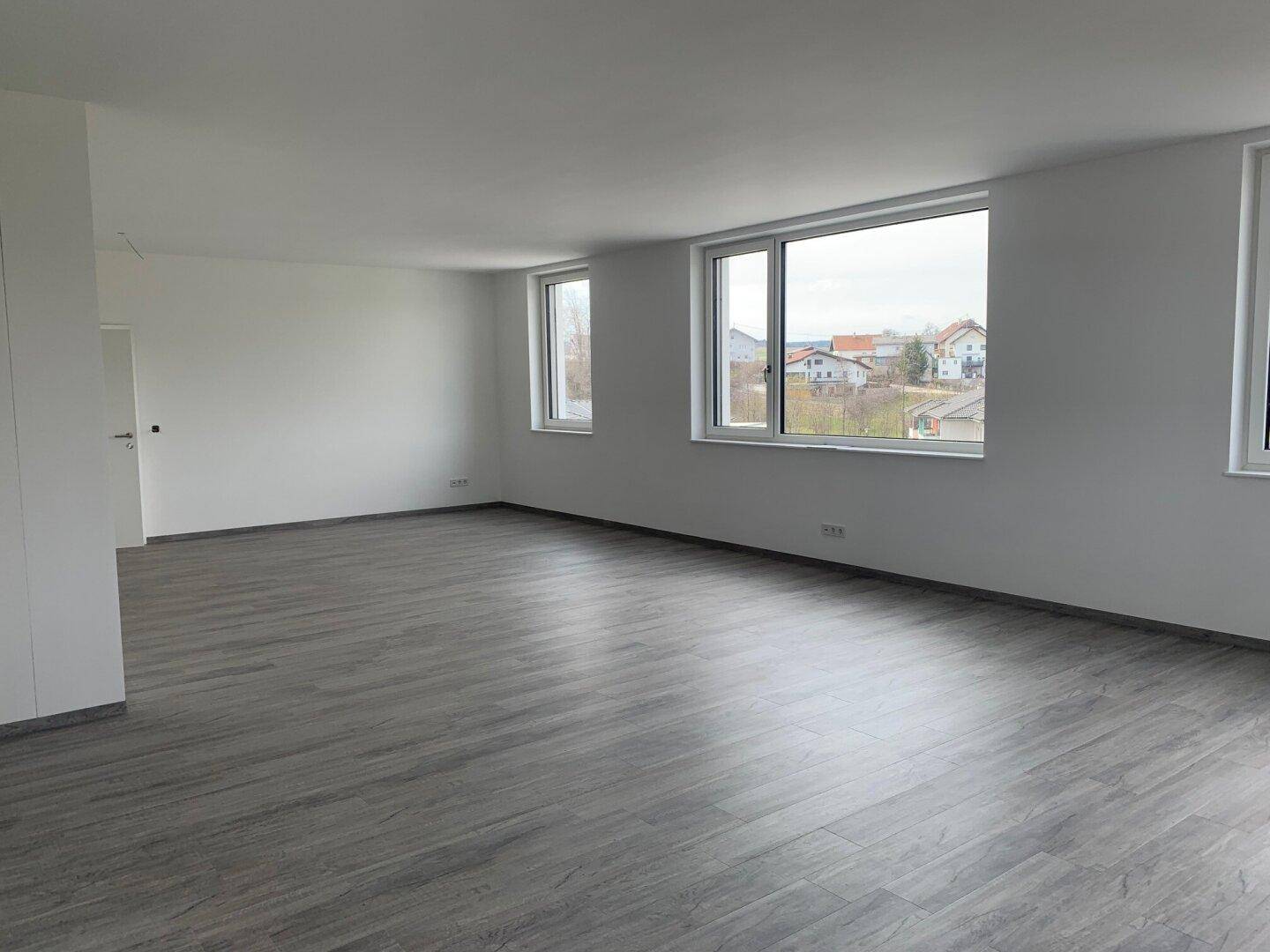 Geräumiger, heller Raum mit grauem Laminatboden und Fenstern, die einen weiten Blick bieten.