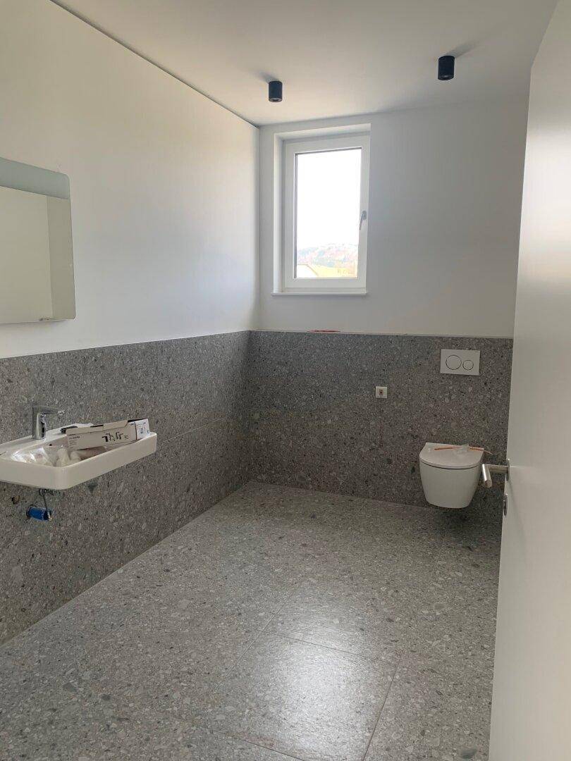 Modernes Badezimmer mit grauen Fliesen an Boden und Wänden, ausgestattet mit Waschbecken und Toilette.