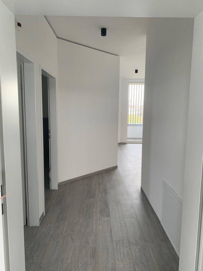 Heller Flur mit grauem Laminatboden, der zu verschiedenen Räumen und einem Balkon führt.