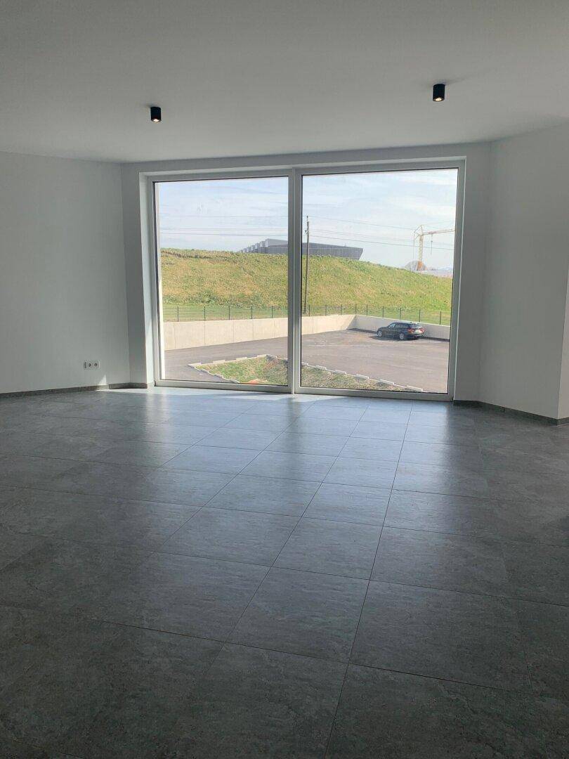 Heller Raum mit modernem Fliesenboden und großer Fensterfront, bietet Blick auf eine begrünte Böschung.