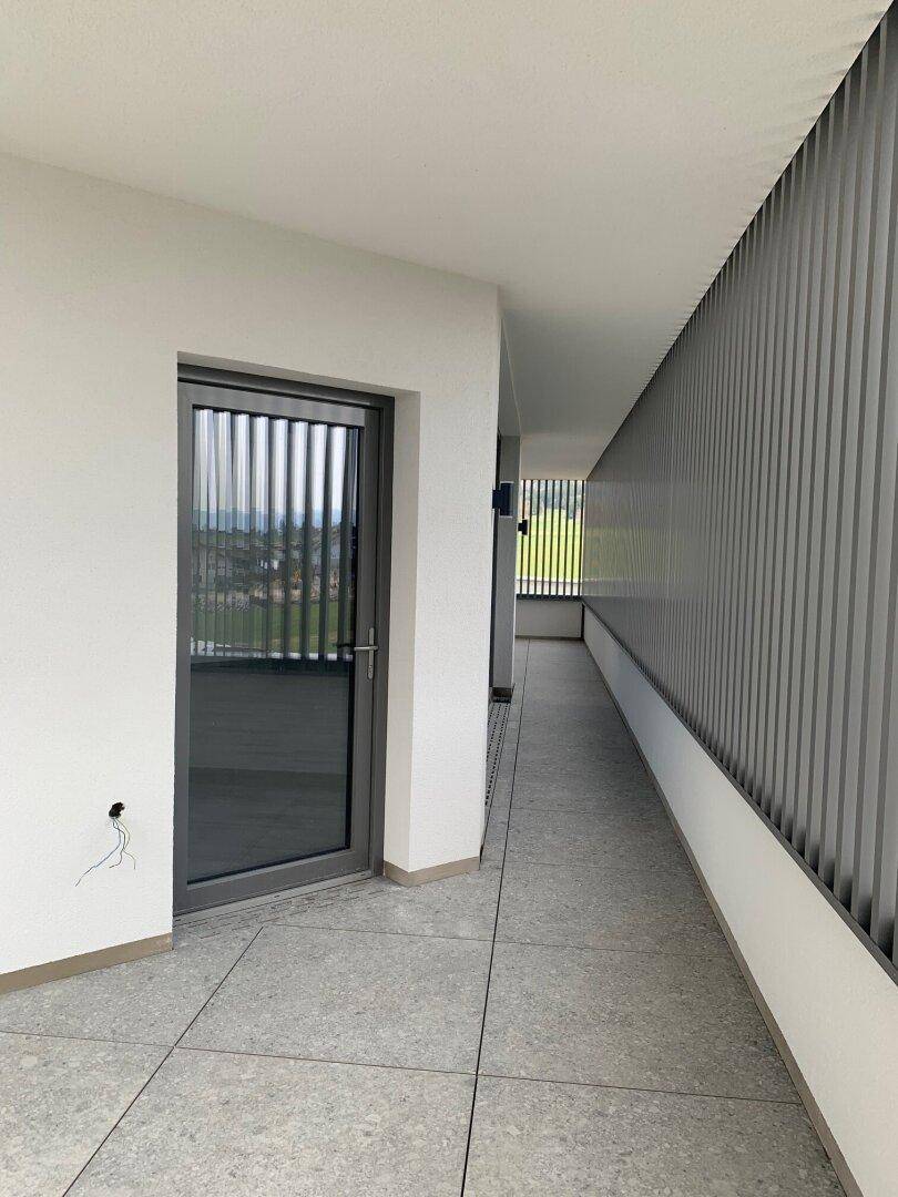 Überdachter Außenbereich mit Fliesenboden und vertikalen Lamellen als Sichtschutz, der einen weiten Blick bietet.