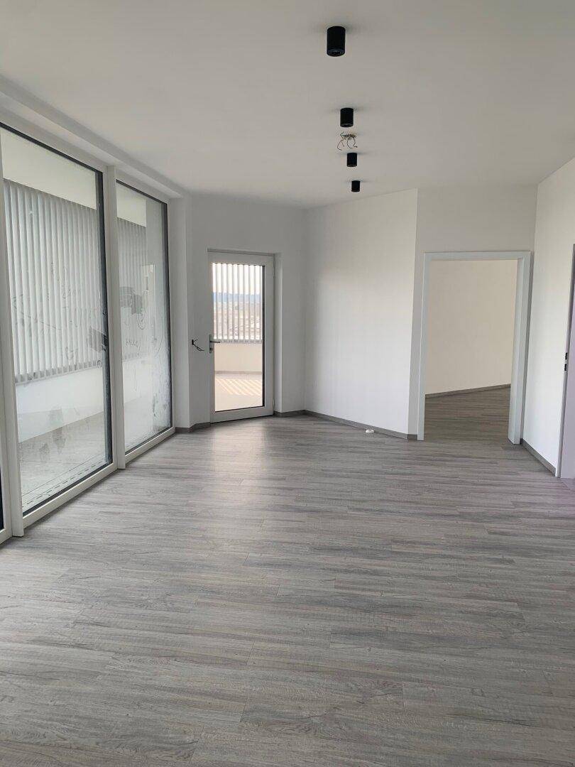 Heller Raum mit großen Fenstern und Zugang zu einem Balkon, ausgestattet mit modernem grauem Laminatboden.