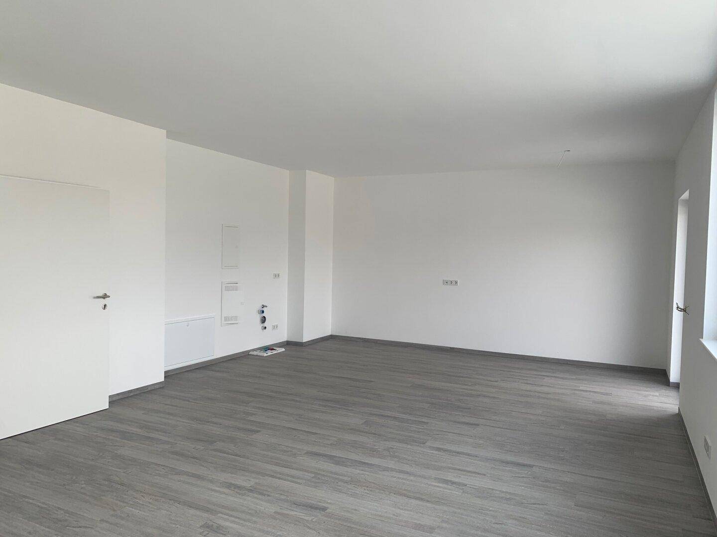 Großer, leerer Raum mit grauem Laminatboden und weißen Wänden, bereit für individuelle Gestaltung und Nutzung.