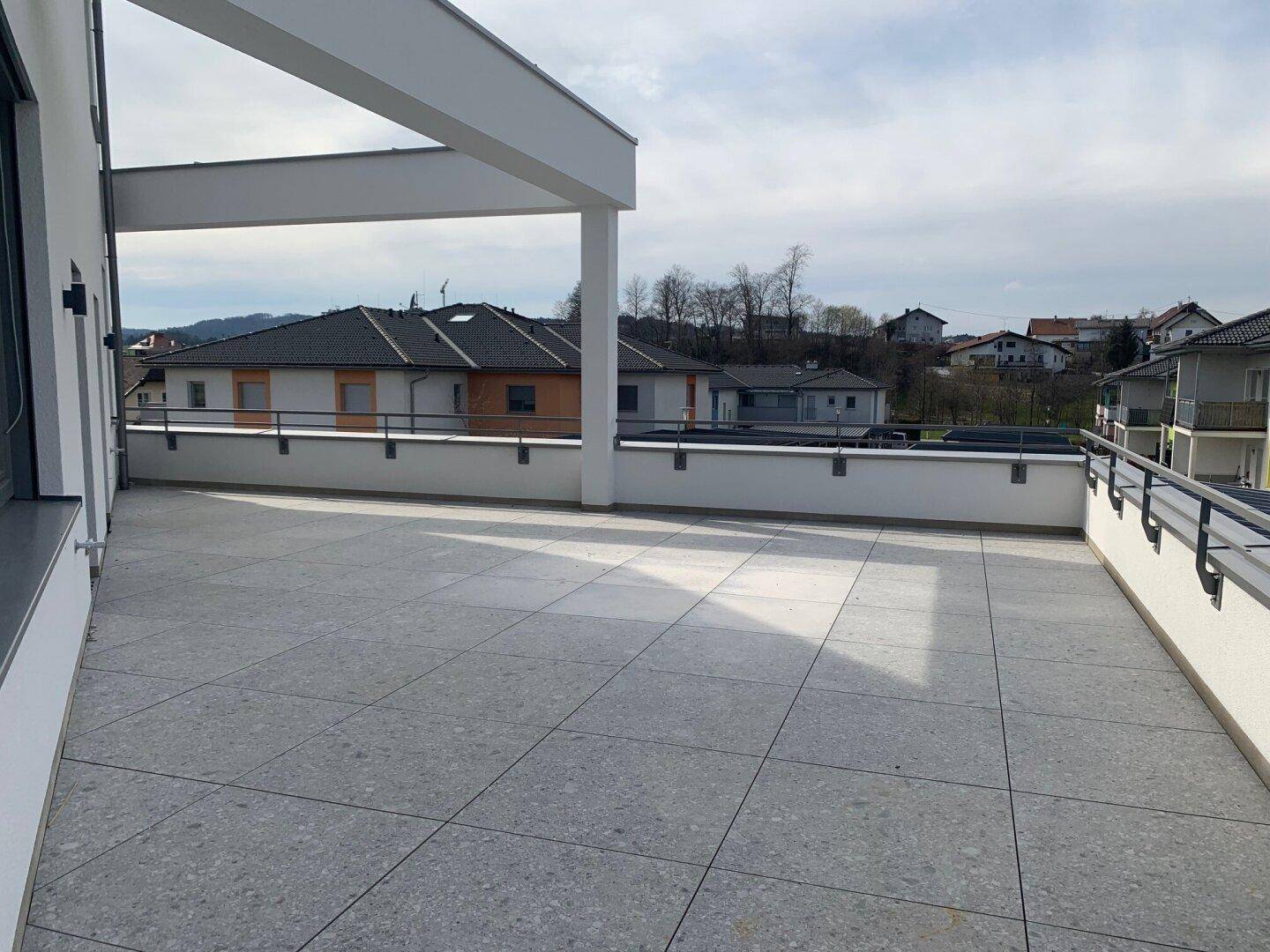 Große Dachterrasse mit Fliesenboden und moderner Brüstung, die einen weiten Blick auf die Umgebung bietet.