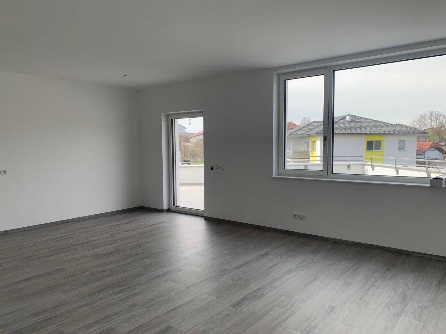 Heller Raum mit grauem Laminatboden und Zugang zu einer Terrasse, der viel Tageslicht hereinlässt.