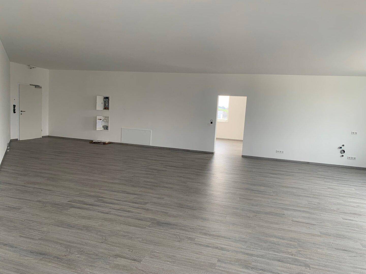 Großer, heller Raum mit modernem Vinylboden und Zugang zu einem weiteren Zimmer, ideal für flexible Nutzung.