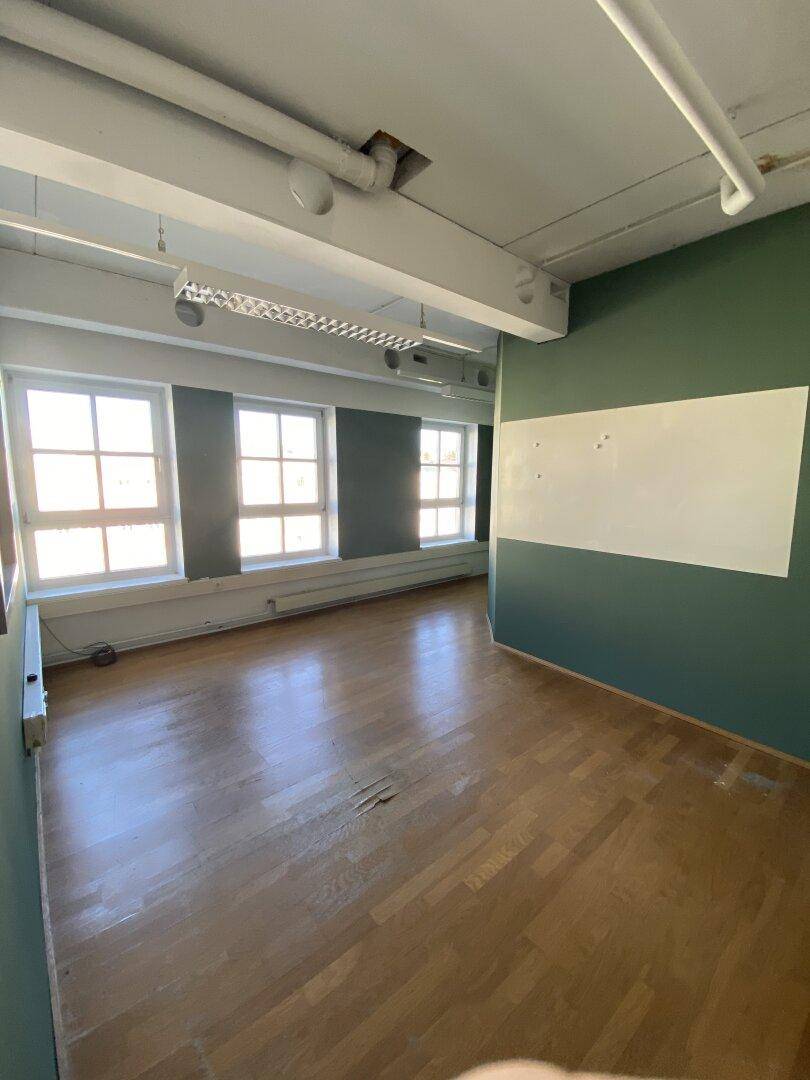 Büro mit Holzboden, grünen und weißen Wänden und drei Fenstern, die viel Tageslicht hereinlassen.