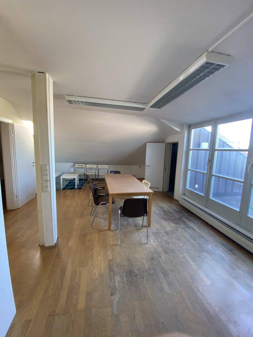 Geräumiges Büro im Dachgeschoss mit Holzboden, einem langen Tisch und Zugang zu einer Terrasse.