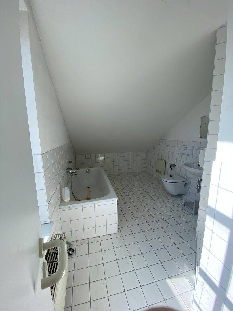 Badezimmer im Dachgeschoss mit Badewanne, WC, Waschbecken und weißen Fliesen an Wänden und Boden.