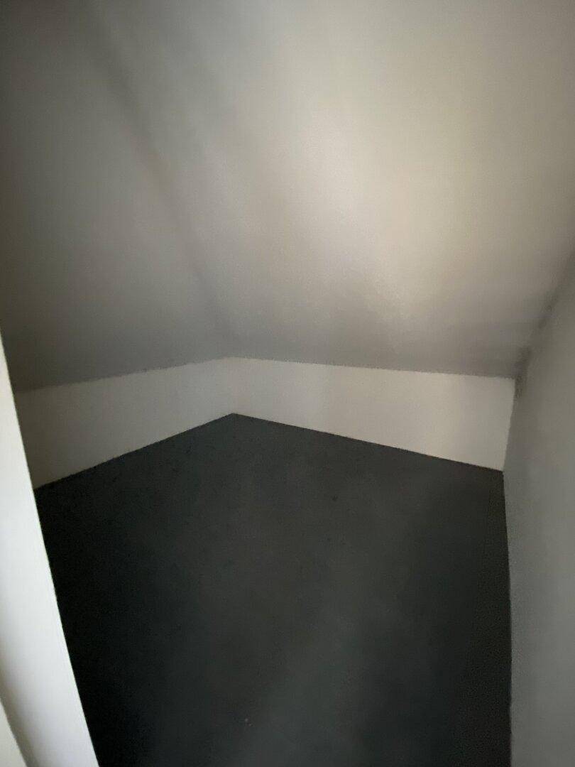 Kleiner Abstellraum im Dachgeschoss mit schrägen Wänden und dunklem Boden, ideal für Lagerzwecke.