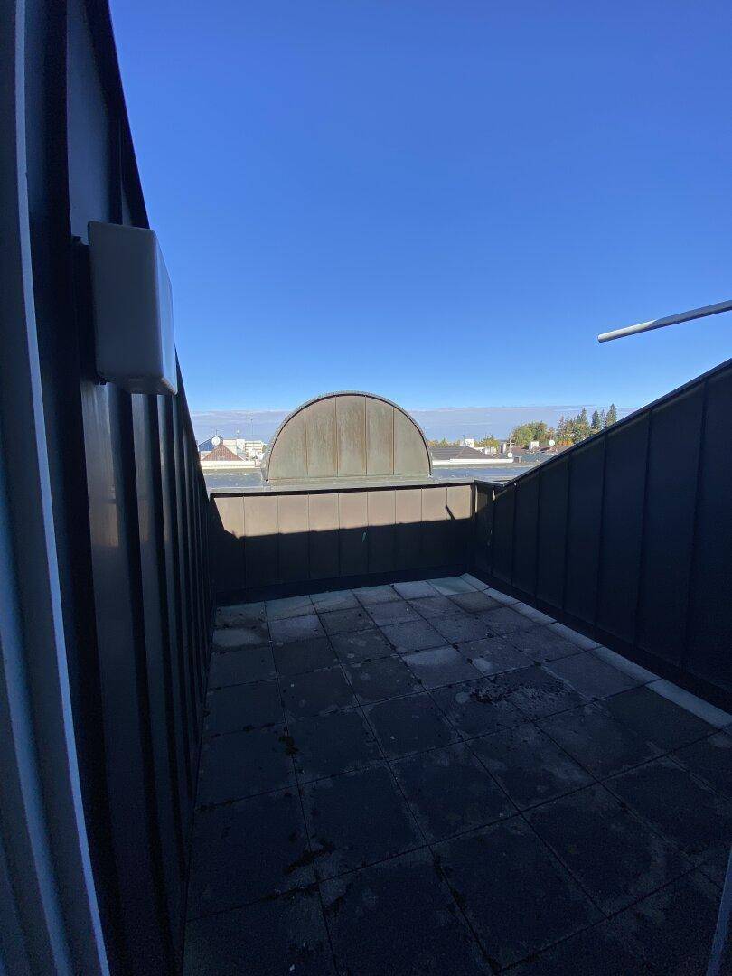 Dachterrasse mit Fliesenboden und Blick auf die umliegenden Dächer und den blauen Himmel.