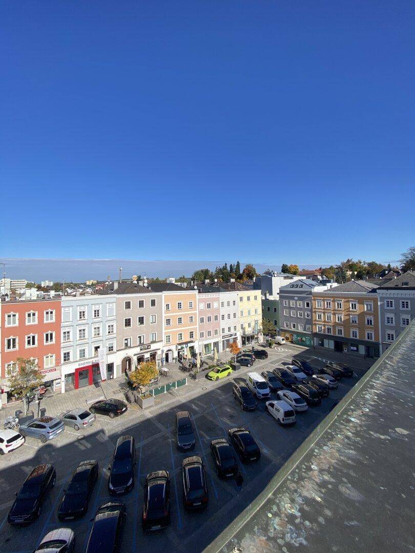 Panoramablick auf eine belebte Stadtlandschaft mit farbenfrohen Gebäuden und einem großen Parkplatz unter blauem Himmel.