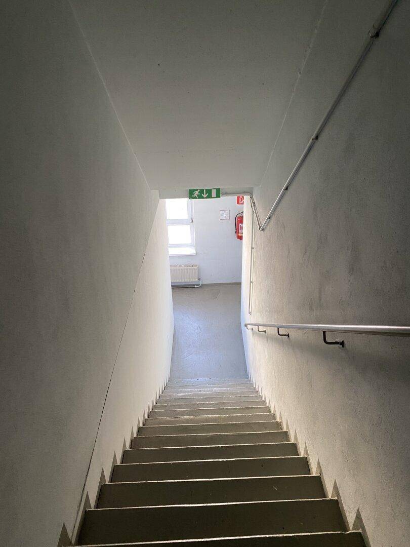 Treppenhaus mit grauen Stufen, weißen Wänden und einem Handlauf, der zu einem oberen Stockwerk führt.