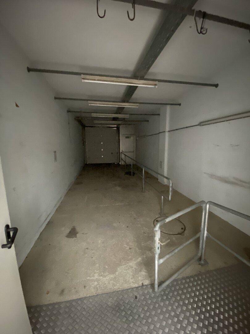 Langer, schmaler Kellerraum mit Betonboden, weißen Wänden und einer Rampe für den Zugang.
