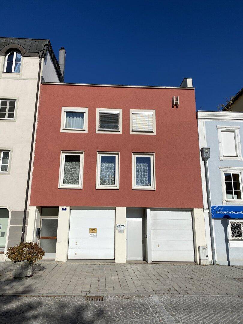 Nahaufnahme einer roten Gebäudefassade mit mehreren Fenstern und zwei Garagentoren im Erdgeschoss an einem sonnigen Tag.