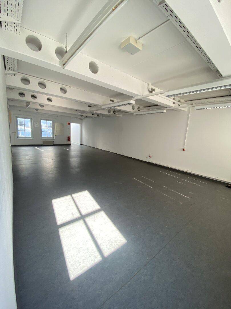 Großer, leerer Ladenbereich mit dunklem Boden, weißen Wänden und sichtbaren Deckeninstallationen.
