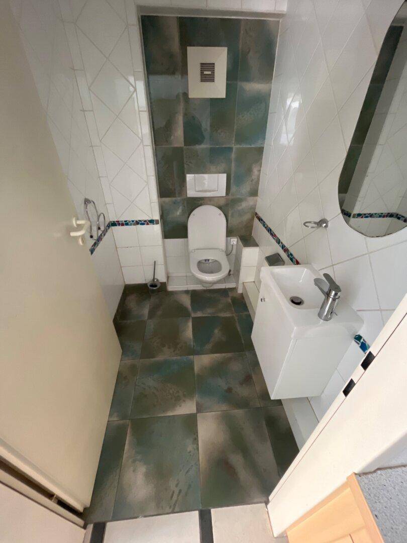 Modernes Gäste-WC mit Wand-WC, kleinem Waschbecken und dekorativen Fliesen in Grün- und Weißtönen.