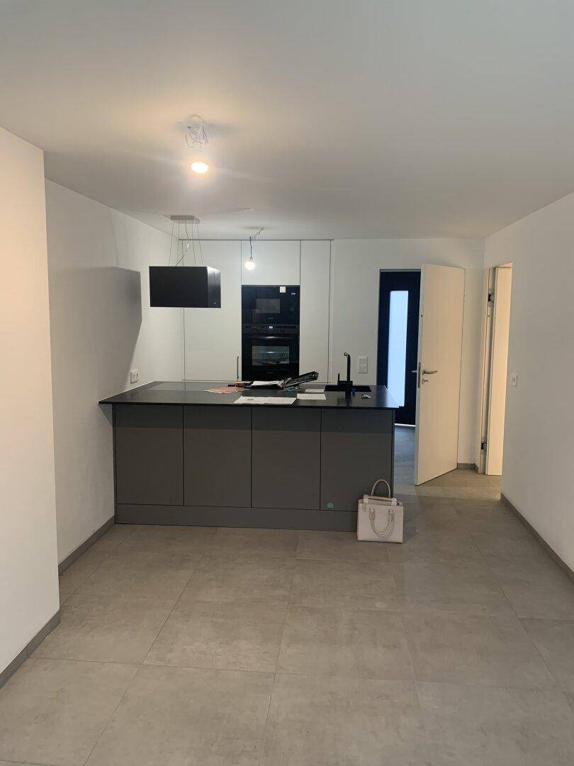 Moderne Küche mit Kücheninsel, dunklen Arbeitsplatten und integrierten Geräten in hellem Raum.