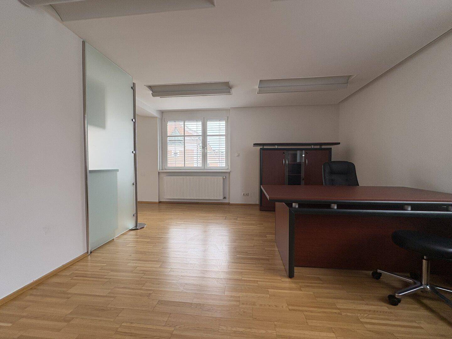 Büro mit Parkettboden, Schreibtisch und einer Milchglaswand, die den Raum optisch abtrennt.
