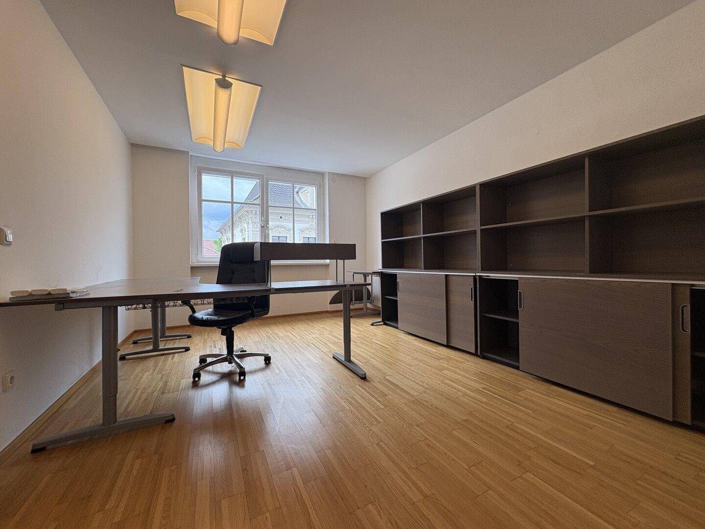 Büro mit Parkettboden, Schreibtisch, Bürostuhl und einer großen Regalwand mit Schiebetüren.