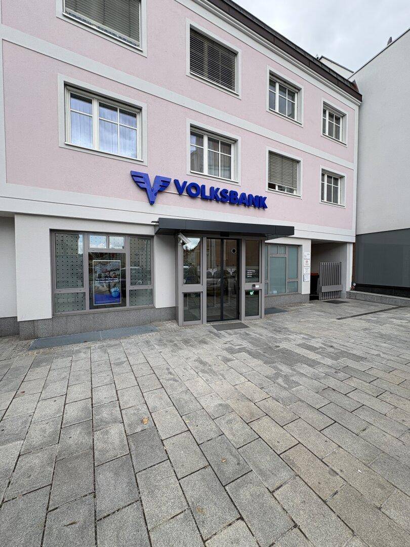 Ansicht der Volksbank-Filiale mit gepflastertem Vorplatz und großen Fenstern im Erdgeschoss.