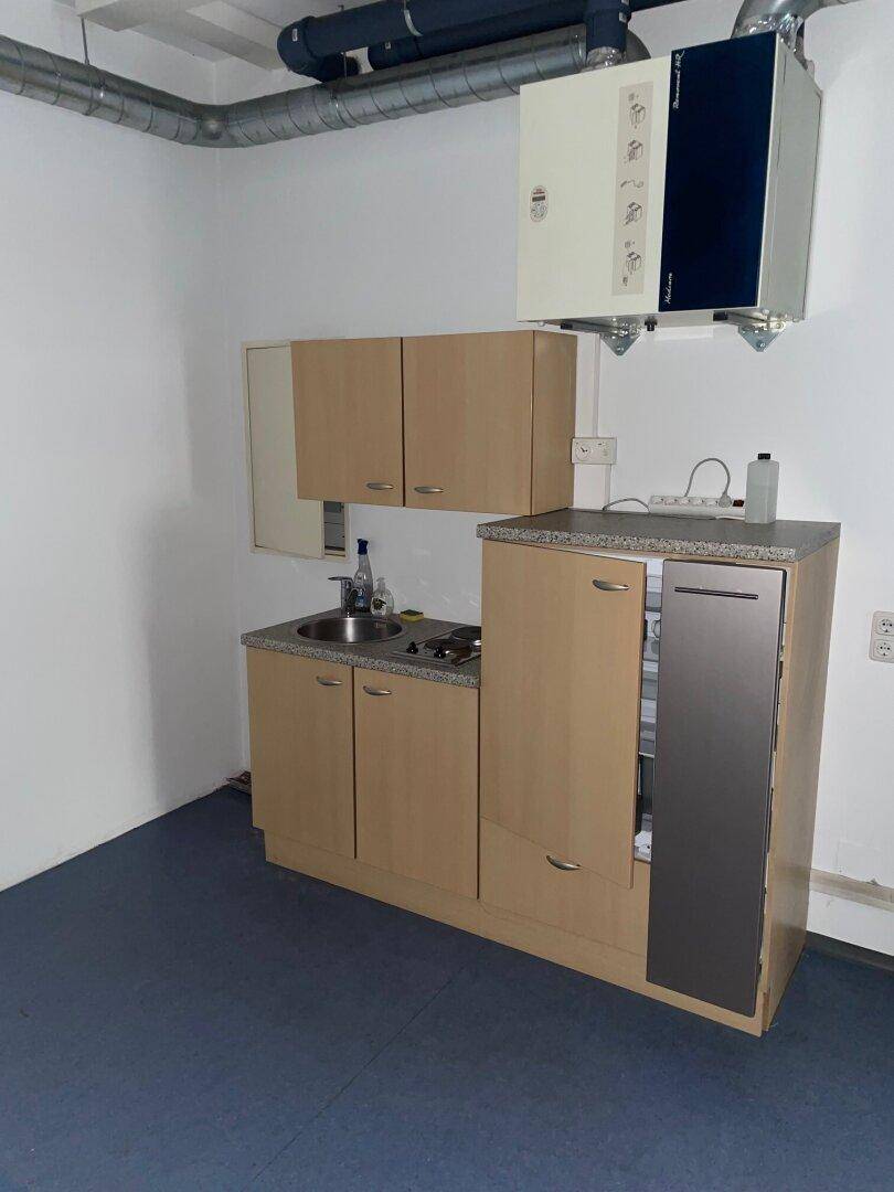 Kleine Küchenzeile mit Spüle, Kochfeld und Kühlschrank in einem Gewerberaum.