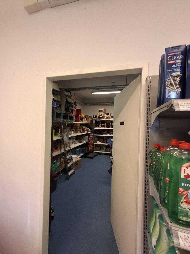 Blick durch eine Tür in einen Lagerraum oder hinteren Bereich des Mini-Marktes mit Regalen und Produkten.