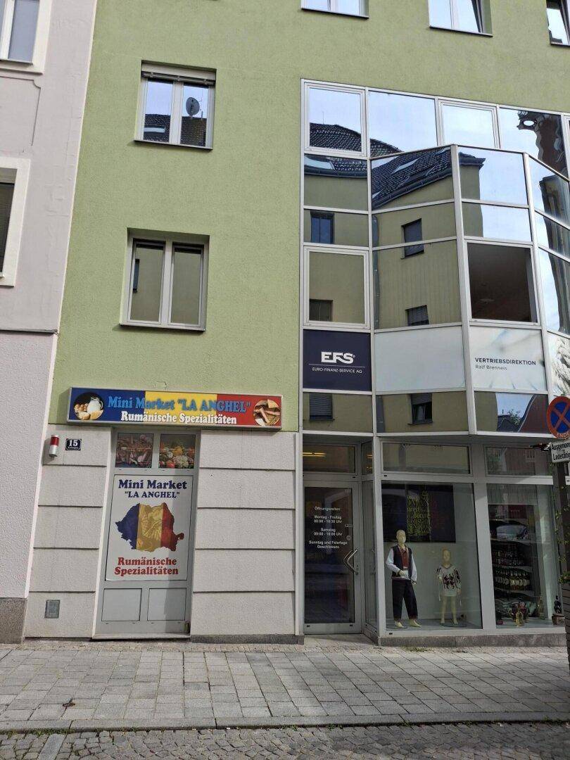Gebäudefassade mit einem Mini-Markt im Erdgeschoss und einem modernen Bürogebäude mit Glasfront daneben.