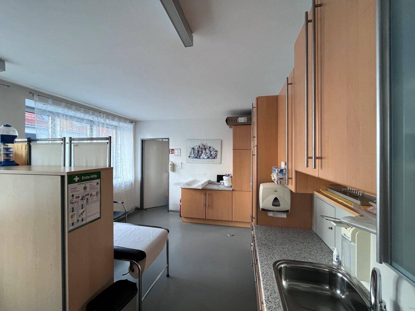 Funktionaler Untersuchungsraum mit Waschbecken, Holzschränken und viel Stauraum.
