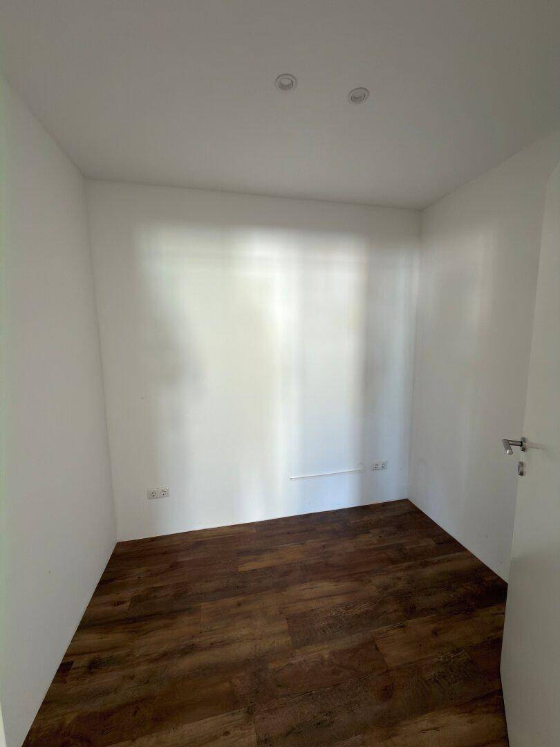 Kleiner, heller Raum mit Holzboden und einem Fenster, das für Privatsphäre sorgt, ideal als Abstellraum oder kleines Büro.