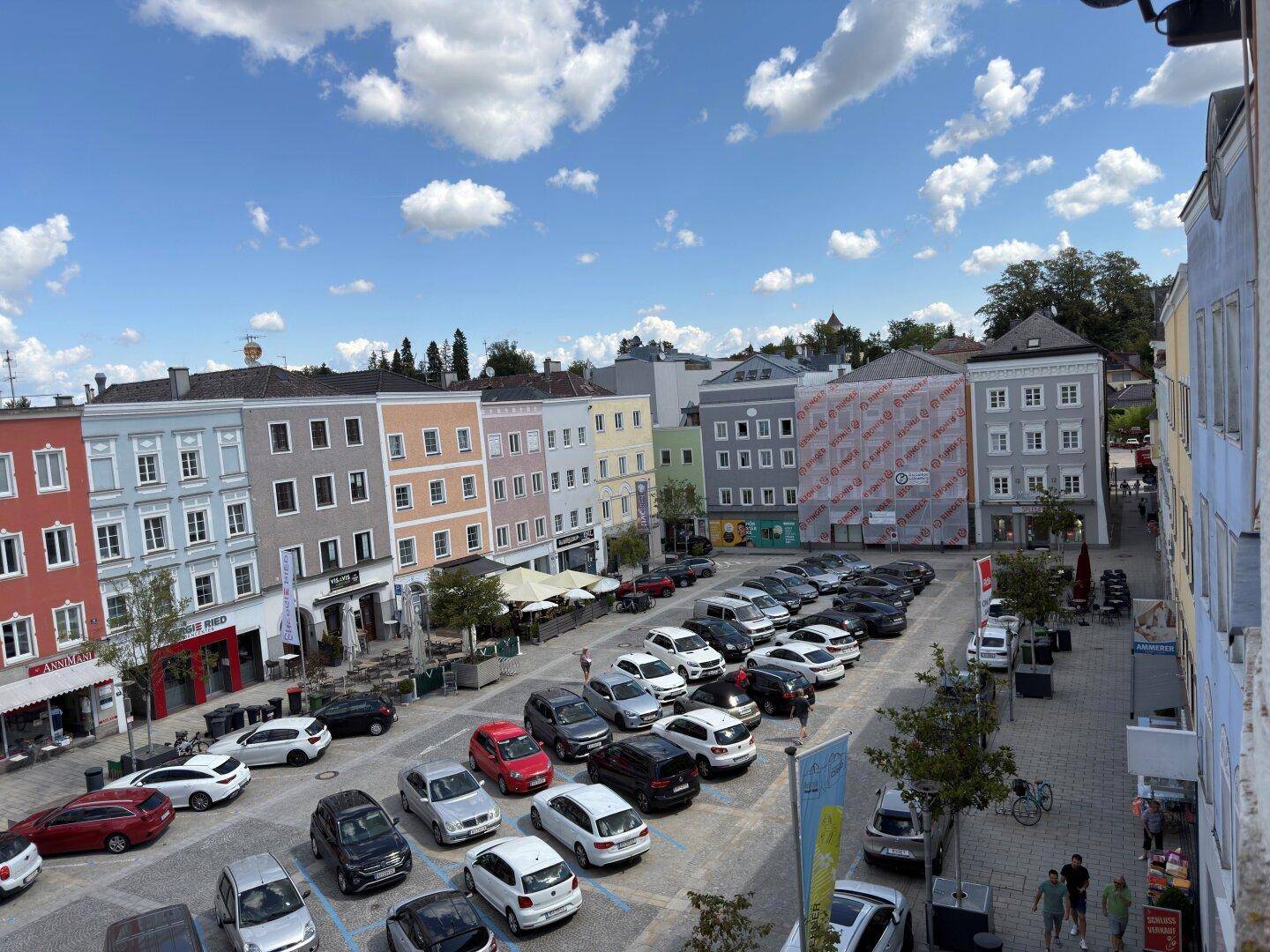 Weitläufiger Blick auf einen Stadtplatz mit zahlreichen parkenden Autos, umgeben von farbenfrohen Gebäuden.
