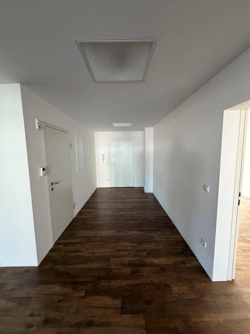 Langer, heller Flur mit Holzboden und weißen Wänden, der zu verschiedenen Räumen und dem Eingangsbereich führt.