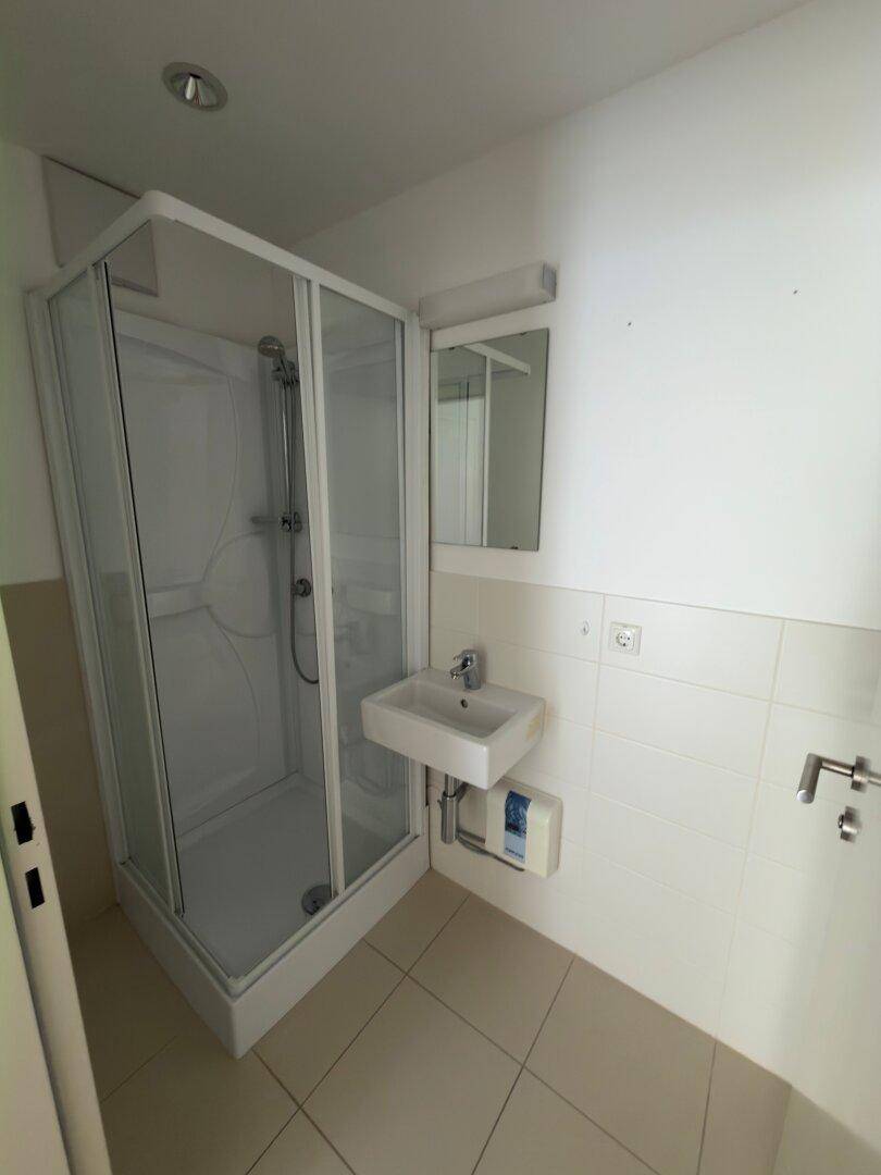 Helles Badezimmer mit Duschkabine, Waschbecken und Spiegel, ausgestattet mit modernen Fliesen und Armaturen.