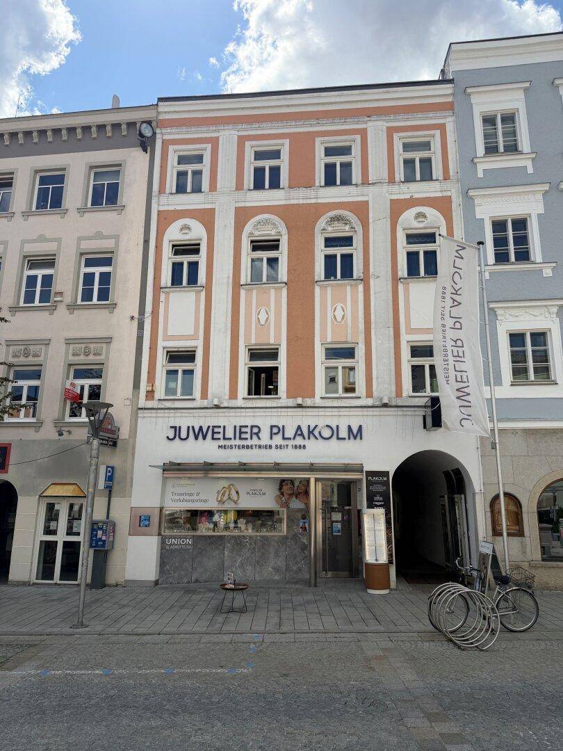 Historische Fassade eines mehrstöckigen Gebäudes mit Geschäften im Erdgeschoss an einer belebten Straße.