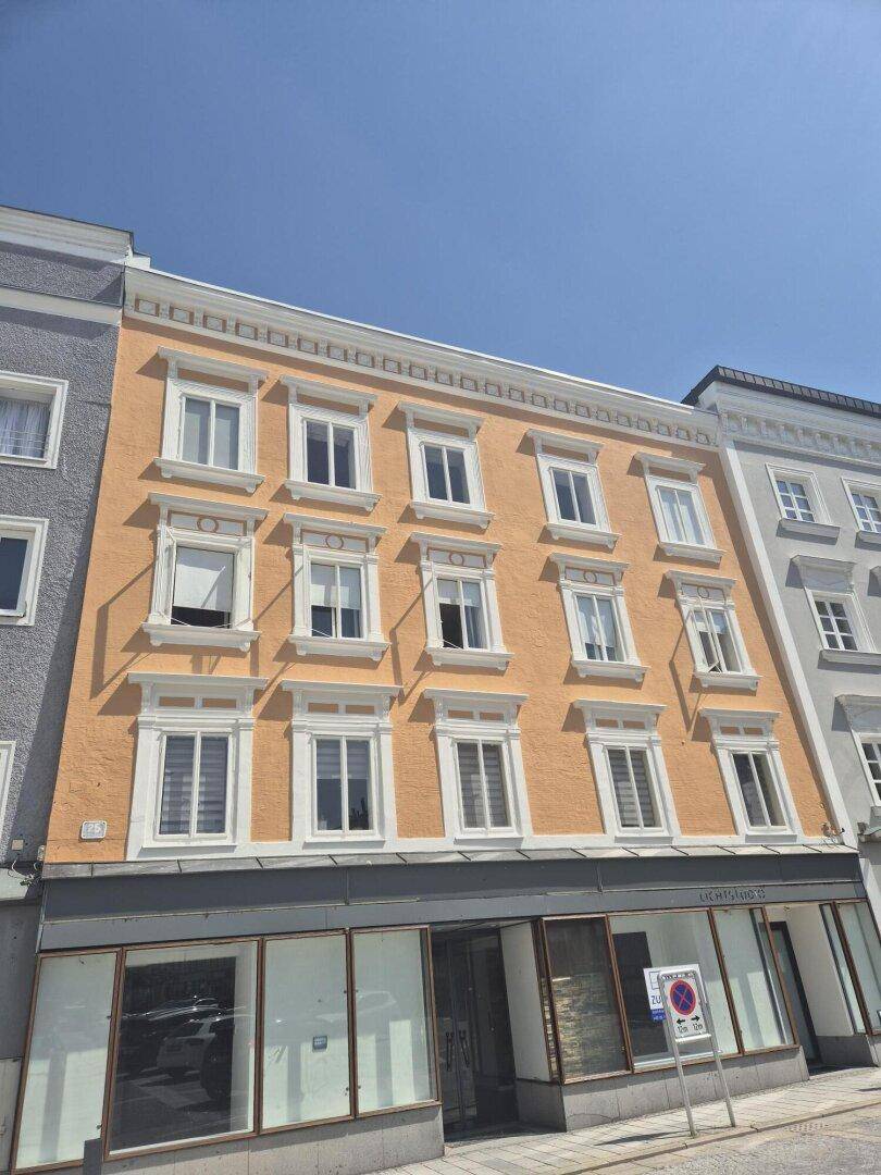 Fassade eines historischen Gebäudes mit orangefarbenem Putz, weißen Fensterrahmen und Ladenlokalen im Erdgeschoss.