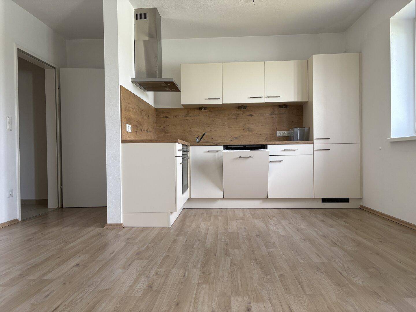 Helle Einbauküche mit modernen Geräten und Laminatboden in offenem Wohnbereich, unbenutzt.