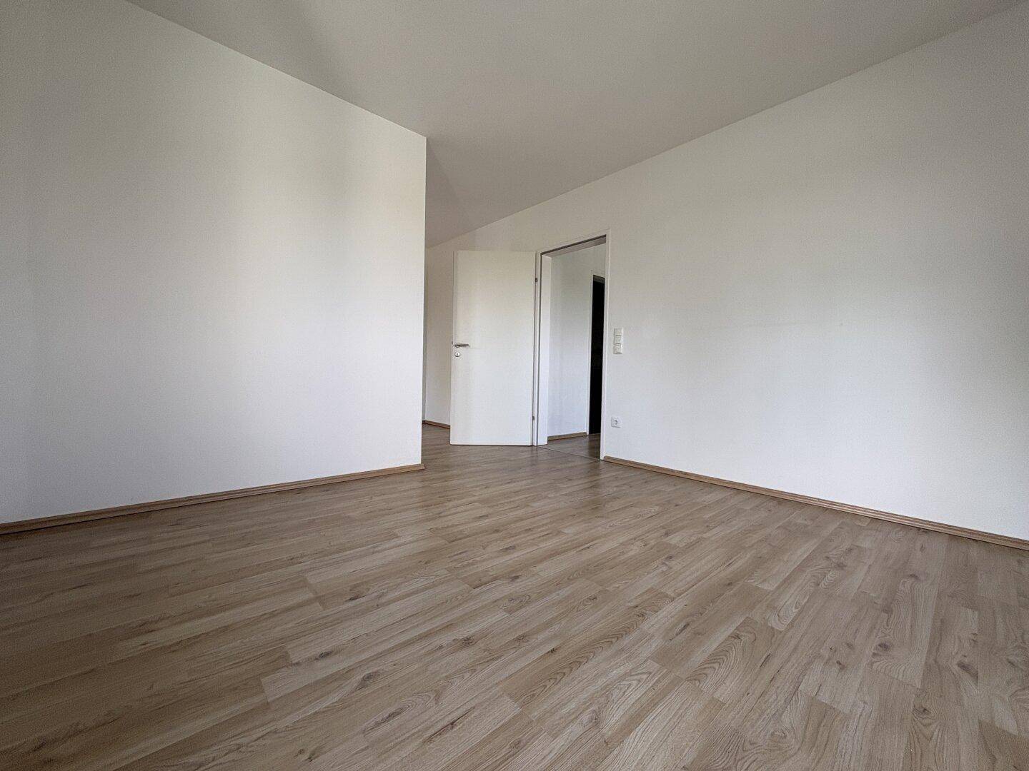 Leerer Raum mit Laminatboden und weiß gestrichenen Wänden, bereit zur individuellen Gestaltung.