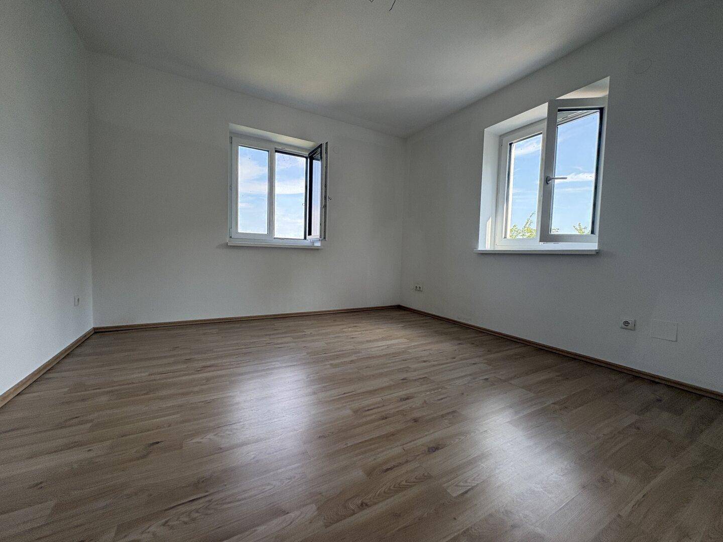 Helles Schlafzimmer mit zwei Fenstern und Laminatboden, ideal für natürliche Belichtung und Ruhe.