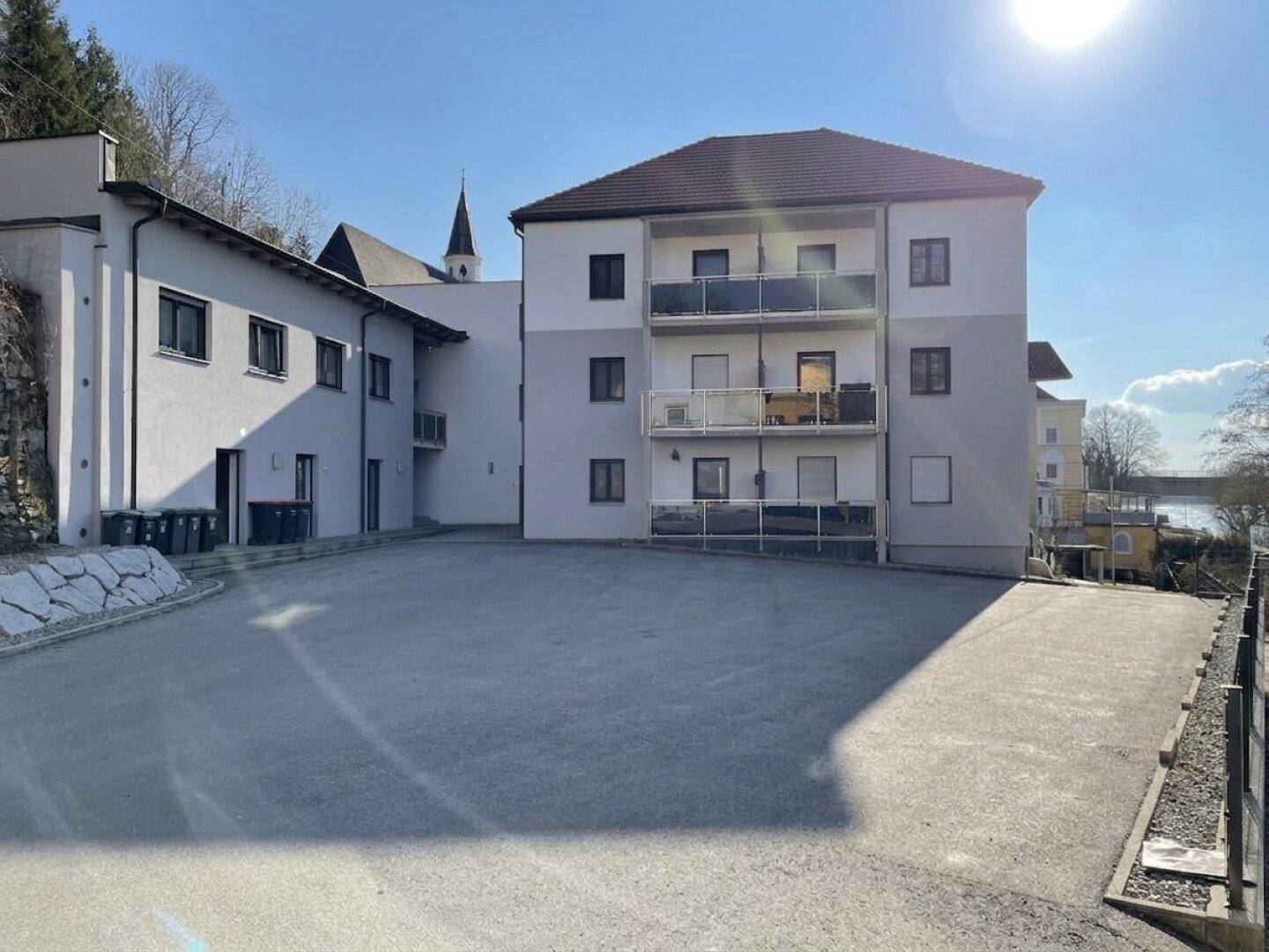 Mehrfamilienhaus mit Balkonen und großem Vorplatz an einem sonnigen Wintertag, gut gepflegt.