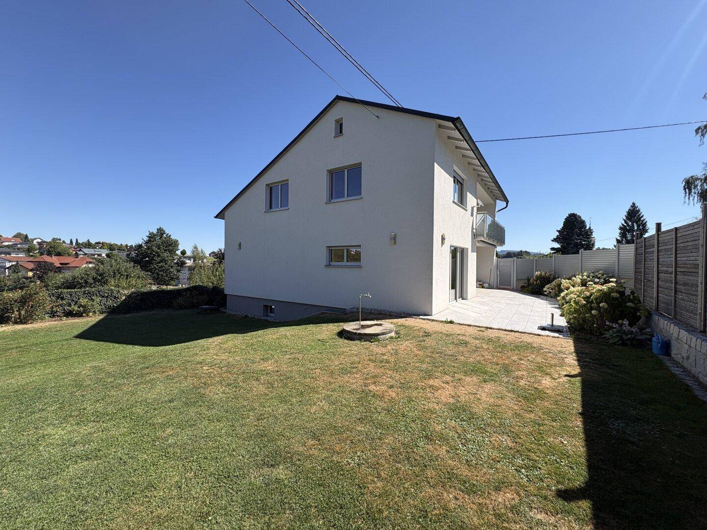 Rückseite des Hauses mit großem Rasen und angrenzender Terrasse unter blauem Himmel.