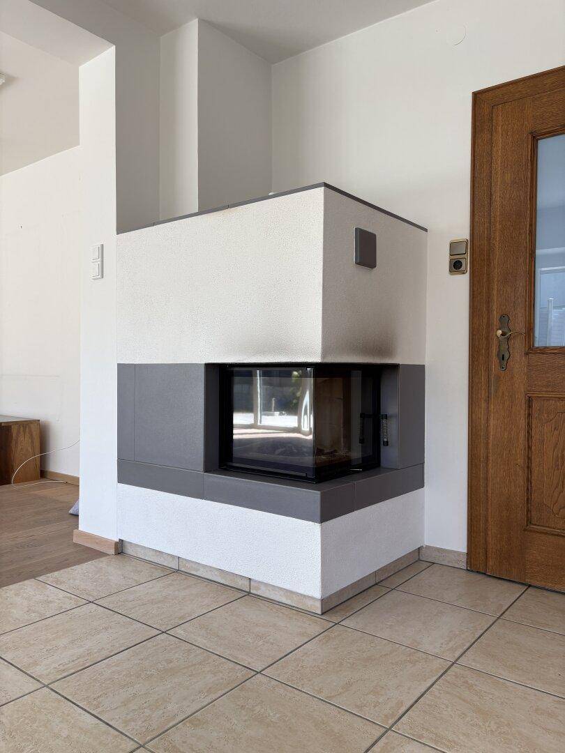 Moderner Kamin mit weißer und grauer Verkleidung neben einer Holztür im Eingangsbereich des Hauses.