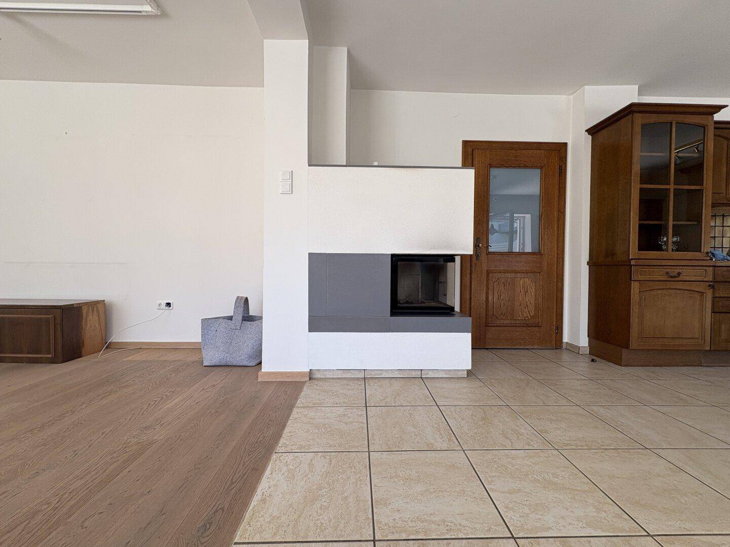 Offener Wohnbereich mit Kamin, Holzboden und Übergang zu einem gefliesten Küchenbereich.