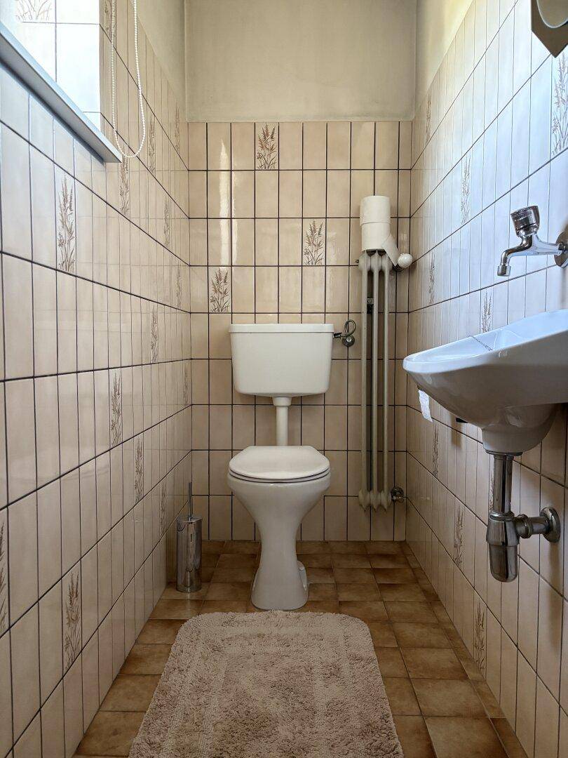 Kleines Gäste-WC mit beigen Fliesen, Fenster und einem einfachen Waschbecken für Besucher.