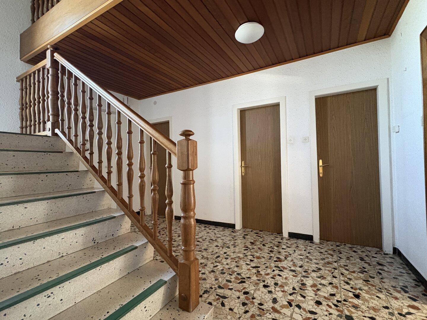 Geräumiger Flur mit Holztreppe, Terrazzoboden und Holztäfelung an der Decke.