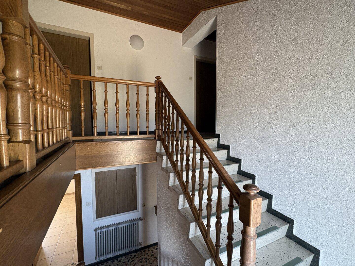 Geräumiges Treppenhaus mit Holzgeländer, Terrazzoboden und Zugang zu verschiedenen Etagen des Hauses.