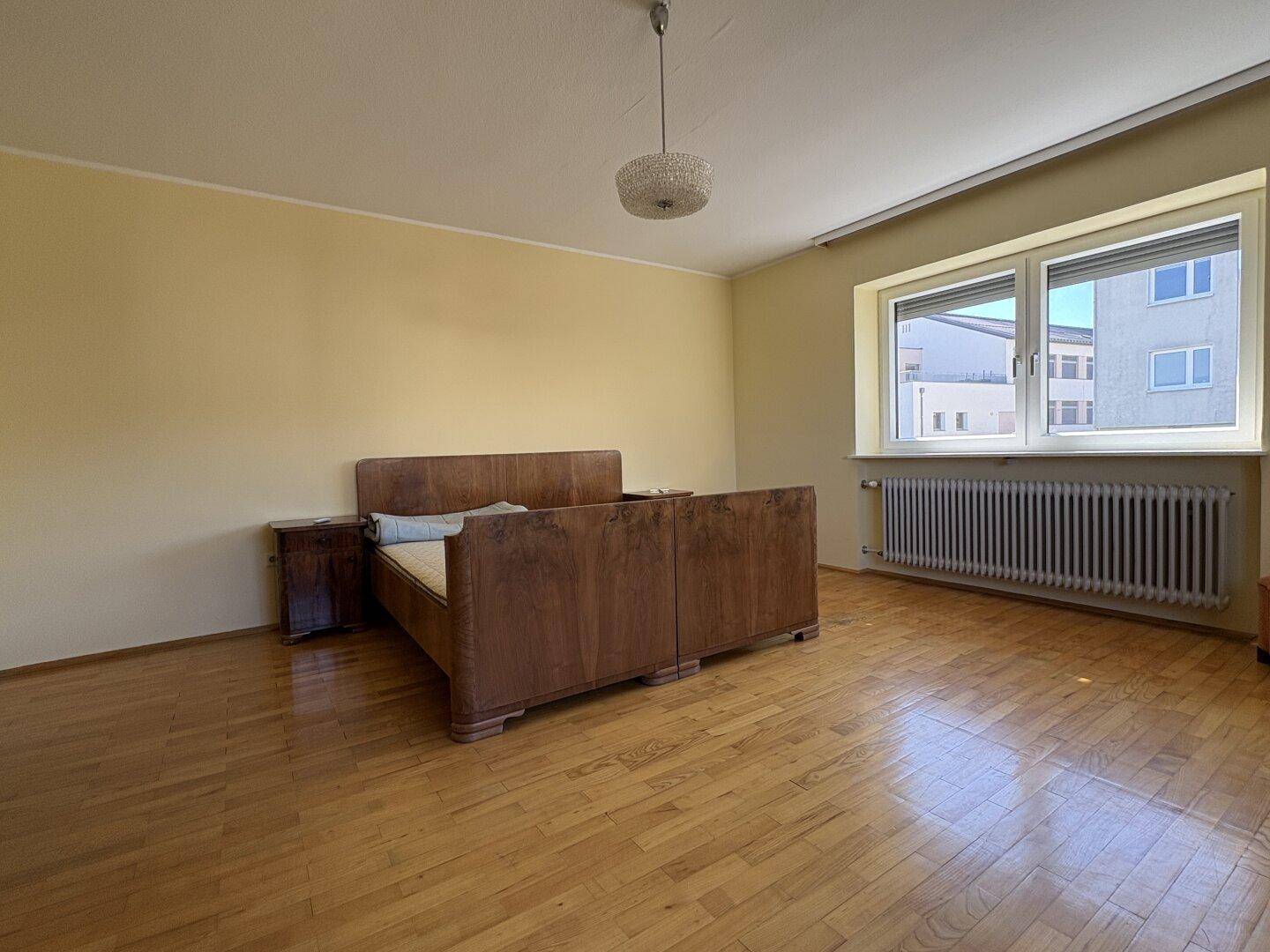 Schlafzimmer mit Parkettboden, einem klassischen Holzbett und großen Fenstern für viel Licht.